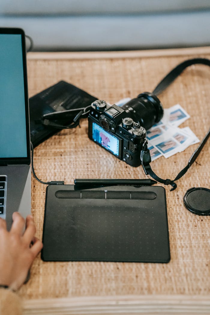 High angle of crop anonymous designer with netbook near graphics tablet and professional photo camera on desk